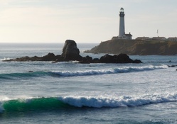 lighthouse above turqoise waves on a rocky beach
