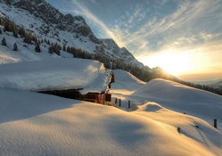 mountain cabin covered in snow at sunrise