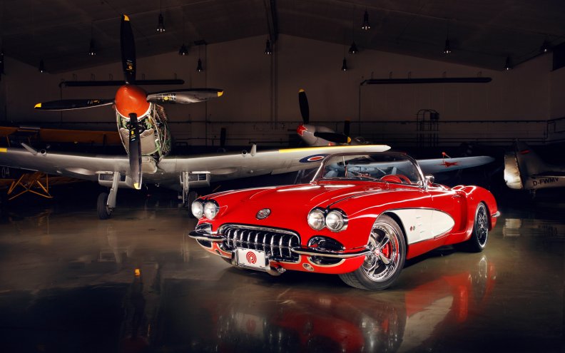 vintage corvette in a hanger with WWII fighters