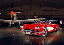 vintage corvette in a hanger with WWII fighters